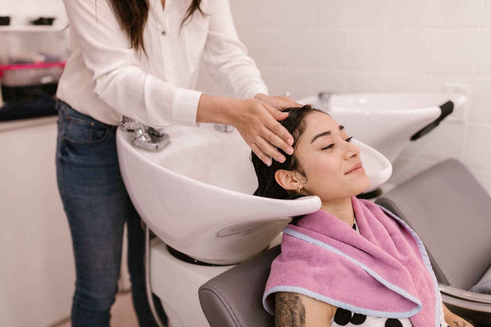 A stylist washing a client's hair at the basin